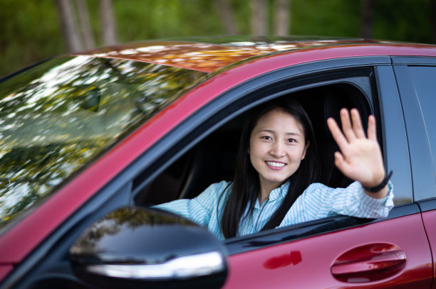 亚洲年轻女子坐在车里，把手伸出窗外，挥手图片下载