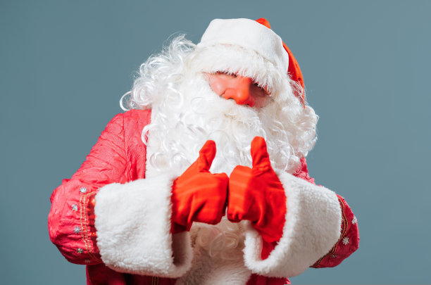 圣诞老人派出生站蓝色背景看镜头拇指向上积极姿态享受节日。图片下载