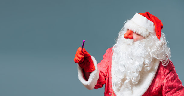 圣诞老人蓝色的画室背景，红色的帽子白色的胡子看相机点到一边用指针。图片下载