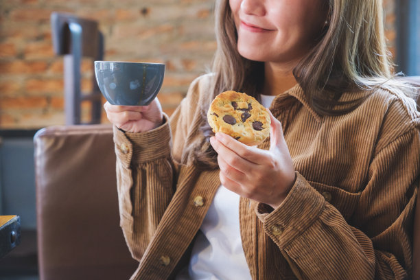 一个年轻女子拿着咖啡杯和一块饼干的特写图像图片下载