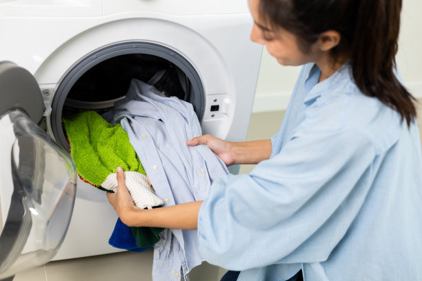 快乐美丽的家庭主妇打开洗衣机的前面，准备在周末把脏衣服放进洗衣机。清洗衣服的女人。图片下载