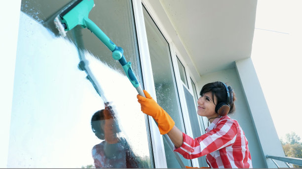 美丽的女人，戴着耳机，戴着手套，清洁，用特殊的拖把擦窗户，享受她的工作，听着音乐。清洁服务工人或家庭主妇图片下载