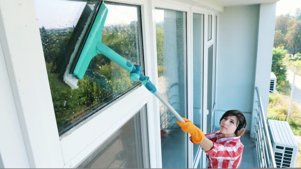 美丽的女人，戴着耳机，戴着手套，在清洁，用特制的拖把擦窗户，享受她的工作，听着音乐。清洁服务工人或家庭主妇图片下载