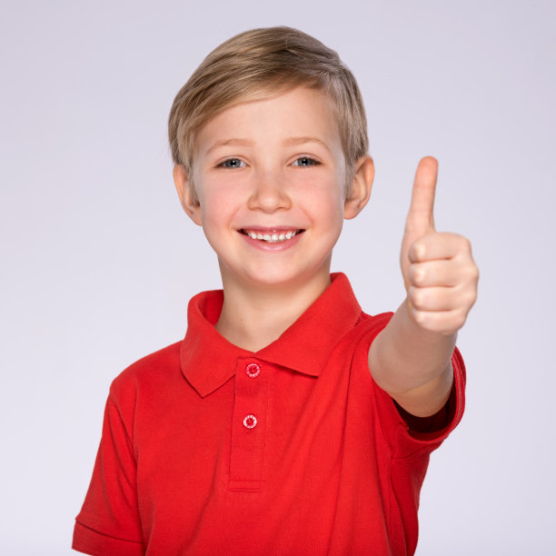 快乐的男孩的肖像显示大拇指的手势，孤立在白色背景。一个穿着红色t恤、竖起大拇指、面带微笑的白人孩子的肖像。有积极情绪的男孩在工作室摆姿势。图片下载