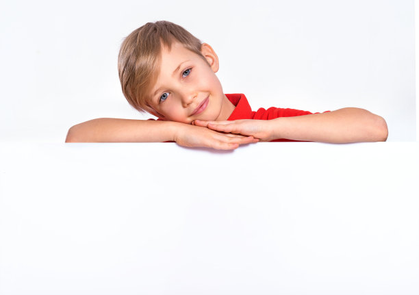 快乐的孩子从空白的广告牌往外看。一个举着白色横幅的快乐男孩的画像。照片上一个快乐的8岁孩子看着相机上方的白纸横幅，孤立的白色图片下载