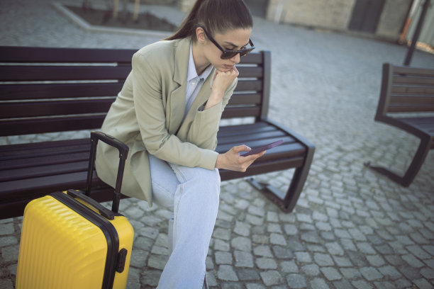 在等待交通工具时，一位提着行李箱的妇女正坐在长凳上休息。图片下载