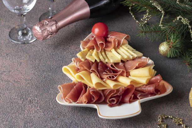圣诞树形盘里的火腿和奶酪开胃菜，棕色背景的香槟和玻璃杯图片下载