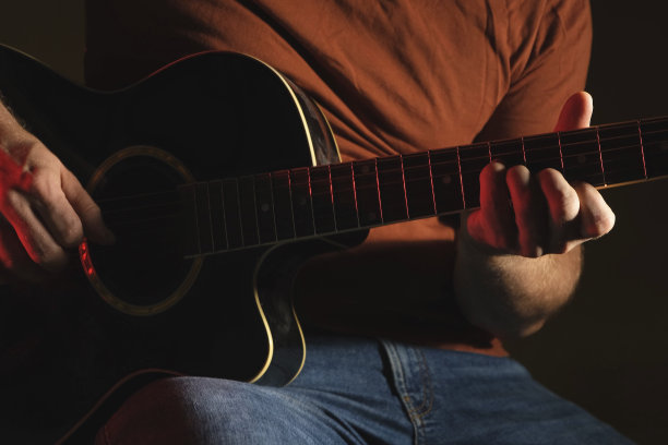 用霓虹灯弹吉他的男人。认不出来人排练。弹奏的吉他。音乐家演奏音乐。男性手指和指板的特写。男人的手在黑暗中弹奏吉他脖子。图片下载