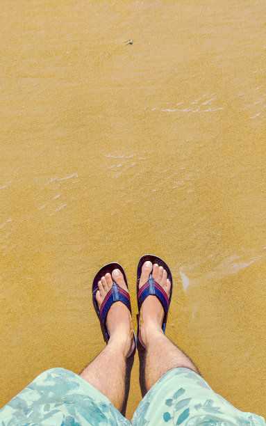 照片的脚凉鞋鞋在沙滩上的沙子背景，顶视图。印度的海滩。图片下载