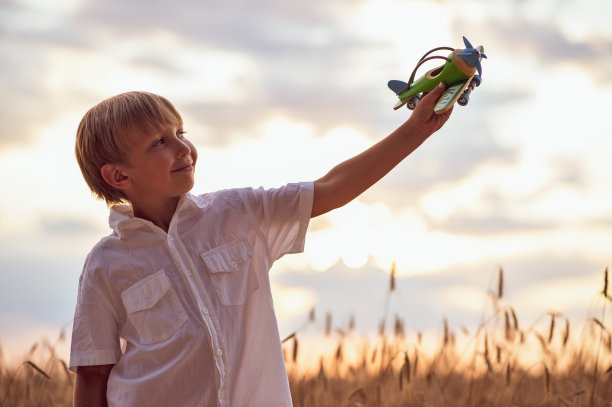 穿着白衬衫的男孩，手里拿着飞机，对着天空。孩子抱着一架木制飞机，梦想成为一名飞行员，在大自然中。夏天日落时分，快乐的孩子在大自然中玩玩具飞机。图片下载