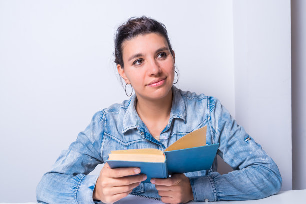 年轻的拉丁妇女，手里拿着一本书，想象着，看着一边。图片下载