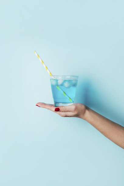 一个蓝色鸡尾酒的特写，在蓝色背景下，一个女性手里拿着一根黄色的管子图片下载