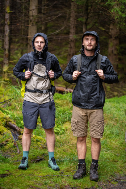 两个穿着雨衣的徒步旅行者在苏格兰的森林里。背包在回来。图片下载