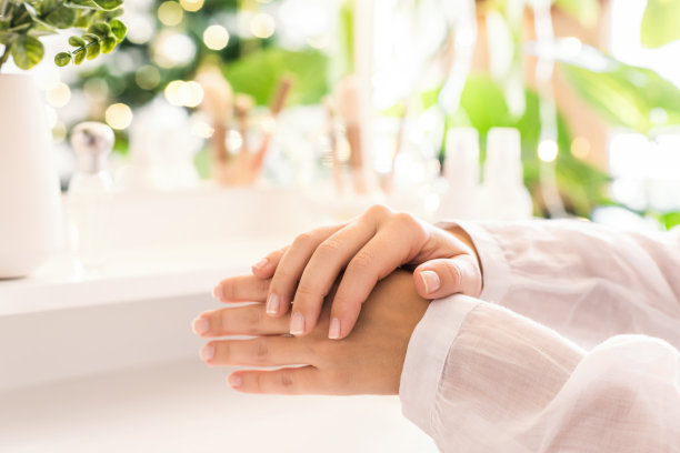 一名妇女在她的手上涂抹每日面霜坐在梳妆台附近与化妆品配件。圣诞树的倒影，桌上镜子里的灯泡。图片下载