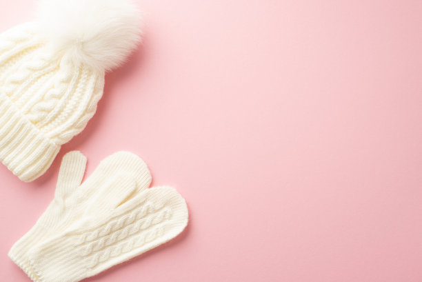 冬季的概念。顶视图照片的白色泡泡帽和针织手套在孤立的淡粉色背景与copyspace图片下载