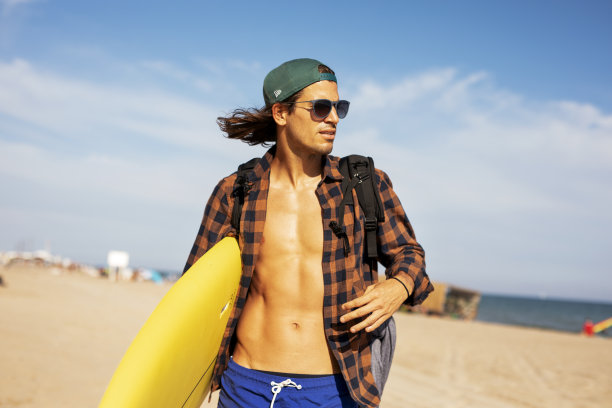 海滩上一个拿着冲浪板的年轻人。图片下载