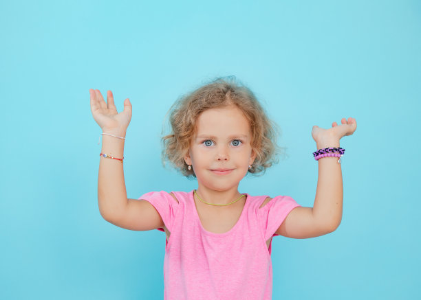 美丽的小女孩展示手工珠首饰空蓝色背景，自由复制空间。快乐的幼儿园年龄的孩子举起手漂亮的手镯。幼稚的配件和美容工艺品图片下载