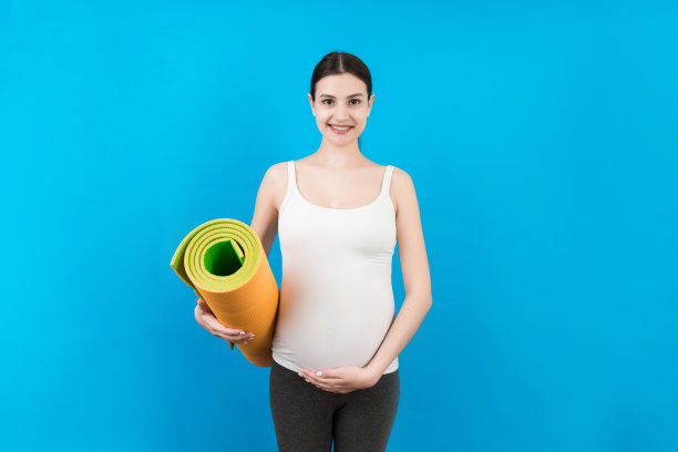 怀孕的女孩抱着瑜伽垫站在彩色背景。工作室拍摄，自由空间的设计图片下载