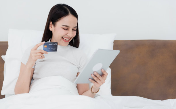 亚洲美女用信用卡用平板电脑通过互联网购物带着快乐的笑容，成为网上购物的新常态在家购物的体验。图片下载