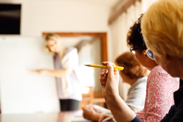 背面三位老年妇女坐在桌前，做笔记，与讲师讨论。演讲者解释策略。图片下载