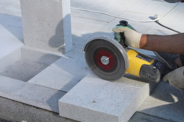 工地上工人用电动磨床修整铺路板。铺设新的人行道瓷砖的概念图片下载