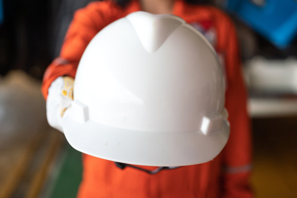 图为，一位建筑工人正在把白色安全帽交给摄像机。图片下载