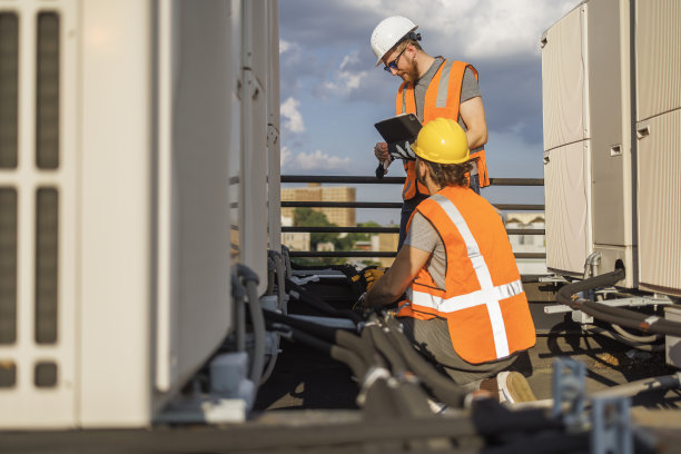 检查屋顶上的空调装置。两个蓝领工人检查空调系统，用便携式电脑记录结果。图片下载