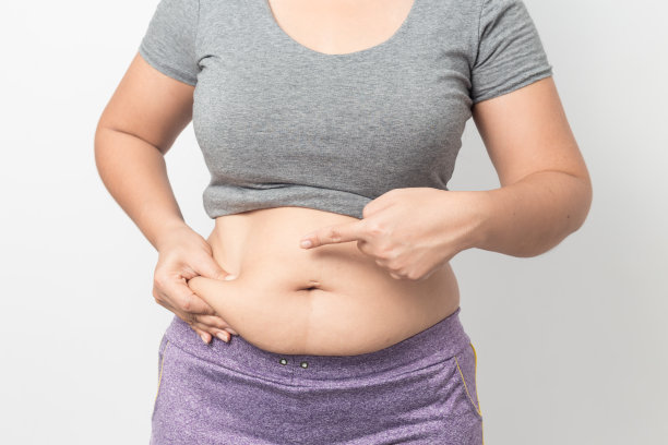 灰色背景下，超重女性手捏腹部多余脂肪，健康概念图片下载