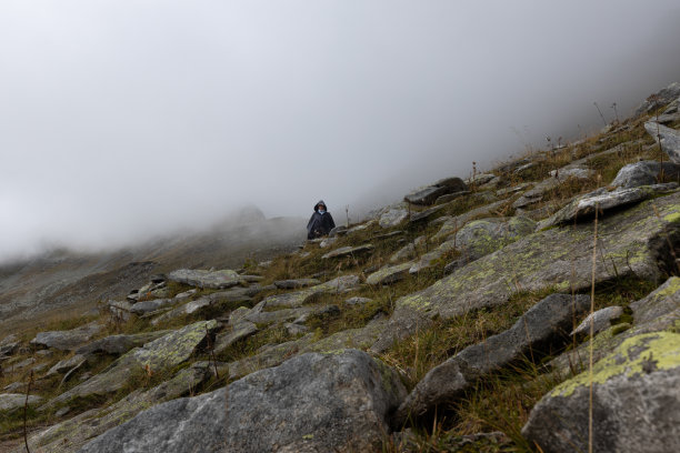 一个穿着雨斗篷的女人走在雾中的山路上。奥地利阿尔卑斯山脉图片下载