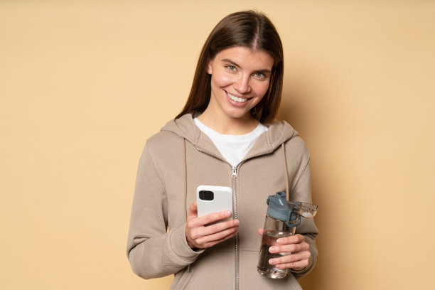 穿着运动帽衫的女子在有氧运动间歇使用手机，手里拿着一瓶水图片下载