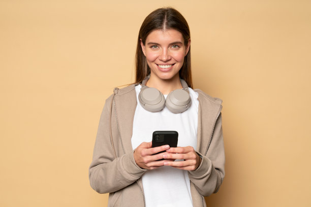 穿着卫衣的女子拿着手机，脖子上戴着无线耳机，使用音乐应用程序下载曲目图片下载