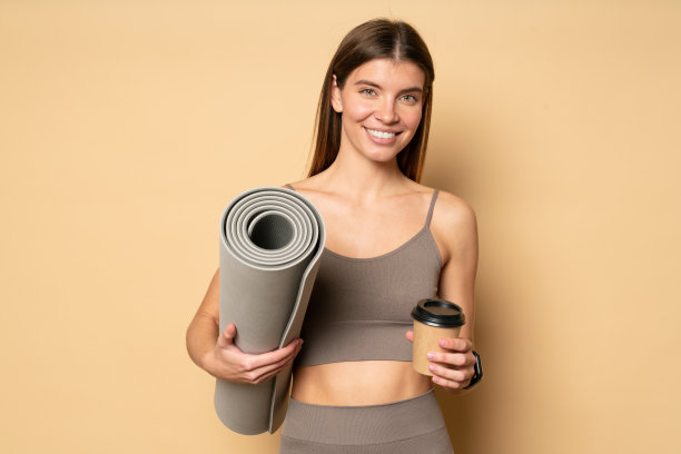 肖像美丽的女人抱着卷垫和咖啡杯后瑜伽练习，孤立图片下载