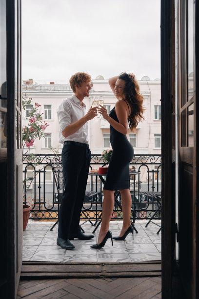 美丽的年轻夫妇站在阳台上拥抱，用香槟敬酒图片下载