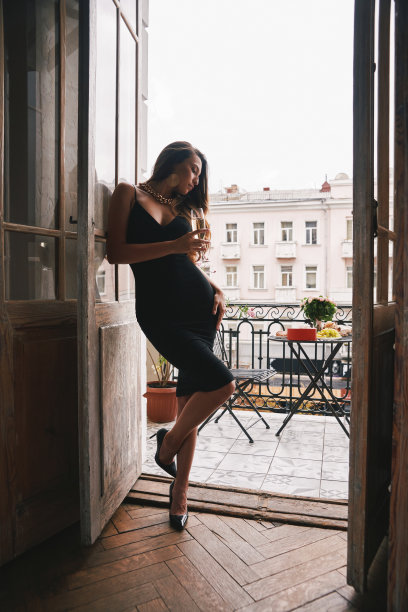 华丽的女人在鸡尾酒礼服手持长笛香槟，而倚靠在阳台的门图片下载