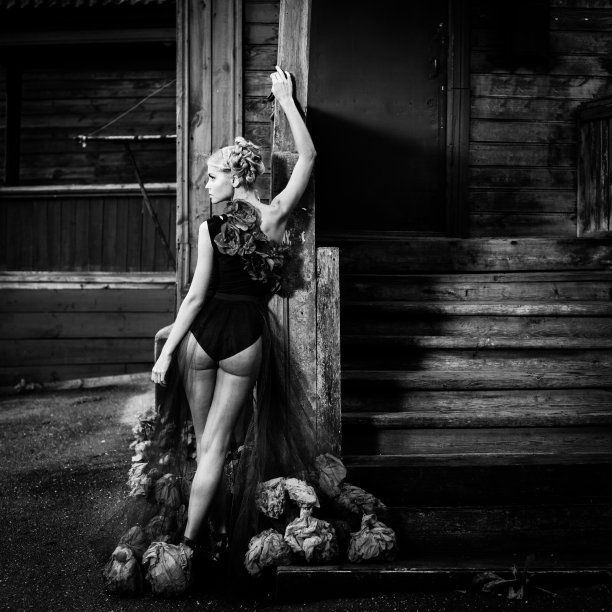 美丽的年轻女子穿着黑色的衣服，带着红色的花，站在老旧腐朽的木楼楼梯附近图片下载