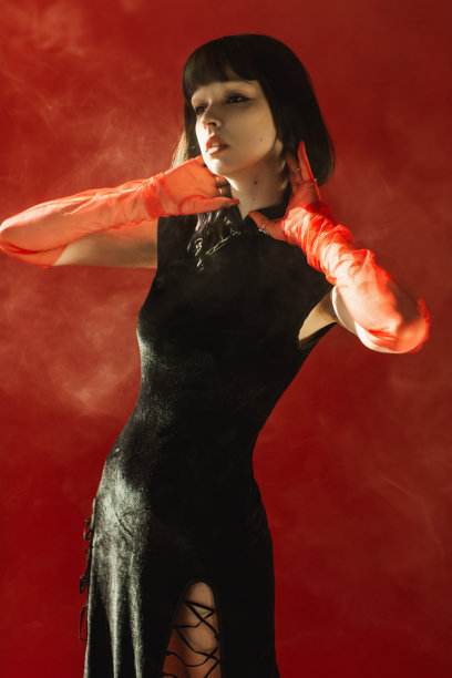 美丽的褐发女子与烟在工作室的红色背景。时尚模特，白皙的皮肤，棕色的头发，黑色的衣服。手套的手。时尚风格。图片下载