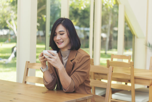 亚洲妇女在绿花园咖啡馆喝黑咖啡。年轻女子微笑着面对爱喝咖啡。美女拿着新鲜的杯子在咖啡店喝黑咖啡。咖啡爱好者图片下载