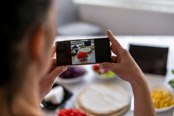 一位年轻的女厨师正在用手机拍摄墨西哥卷饼。图片下载