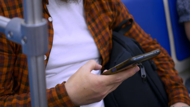 一名男子在公共交通工具上拿着智能手机的手特写，一名男子正在智能手机屏幕上阅读互联网信息。互联网在日常生活中的娱乐套路。图片下载