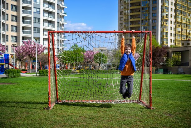 在他家附近的操场上，一个微笑的白人少年挂在一个足球球门上。儿童积极休闲的概念图片下载