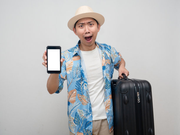 年轻人戴着帽子，穿着沙滩衬衫，带着行李，展示着手机，对假期感到惊讶图片下载