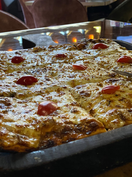 餐厅餐桌的图像设置切片，新鲜烘焙的正方形，玛格丽塔披萨，融化的水牛马苏里拉奶酪，丰富的番茄番茄汁和樱桃番茄一半的顶部，金属叉子，重点在前景图片下载