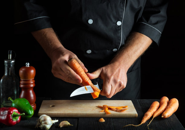 厨师在餐厅的厨房里削胡萝卜皮做蔬菜汤。厨师工作时的特写镜头。胡萝卜的饮食图片下载