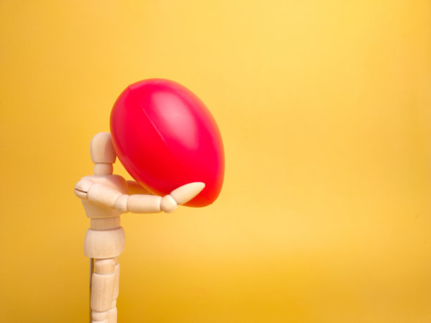 木制假人拿着红色的爱情形状在黄色背景与复制空间。图片下载