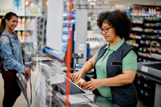 微笑的超市收银员在结账时扫描顾客的杂货。图片下载