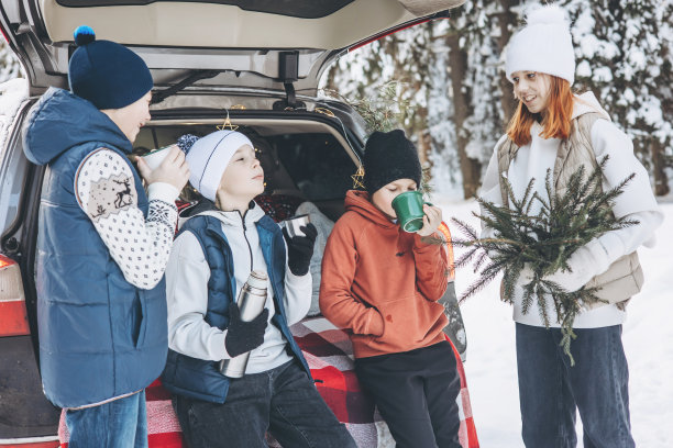 四个朋友十几岁的男孩和女孩坐在汽车后备箱的保温瓶装饰圣诞节和新年。冬天在雪林里野餐。自驾游和当地旅游。朋友们一起出去玩图片下载