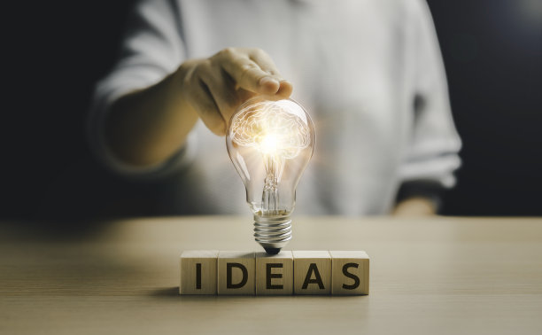 女人的手碰着一个发光的灯泡在木块与文字思想。灯泡。人脑里面的图标。科学和传播概念中的技术创新。图片下载