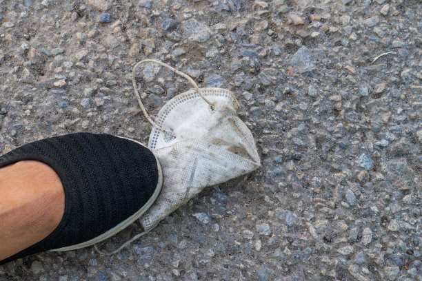 白色肮脏的口罩特写，脚穿着黑色鞋子站在灰色的人行道上图片下载