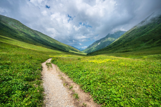 在阳光明媚的日子里，登山驿站在山上，美丽的群山四周被绿色的草和花覆盖着图片下载