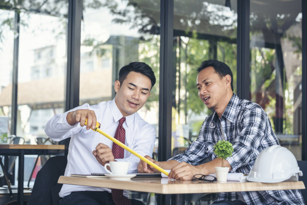 承包商和施工工程师在施工现场的建筑师桌子上开会。业务人员和工程师经理与工头用卷尺讨论施工图。图片下载